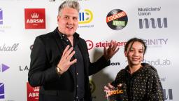 Young woman holding award next to man gesturing with hands